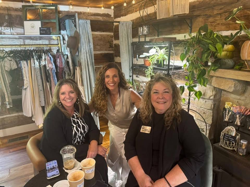 Mayor Lisa Anderson and two other women sit and stand together with coffee drinks inside The Local Grove's rustic, plant-filled interior.