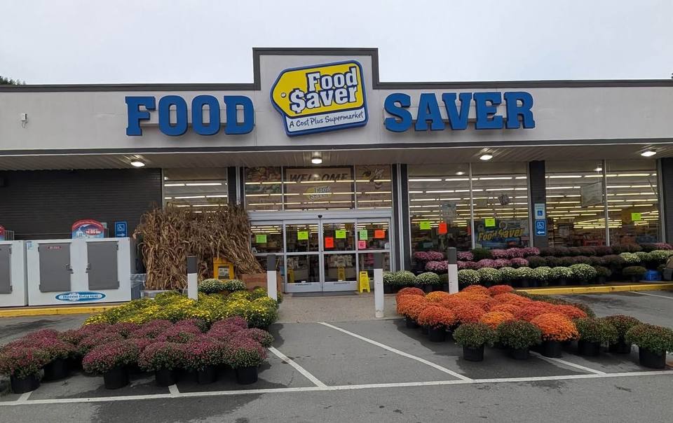 Rows of colorful potted mums in purple, yellow and orange displayed outside the Food Saver storefront.