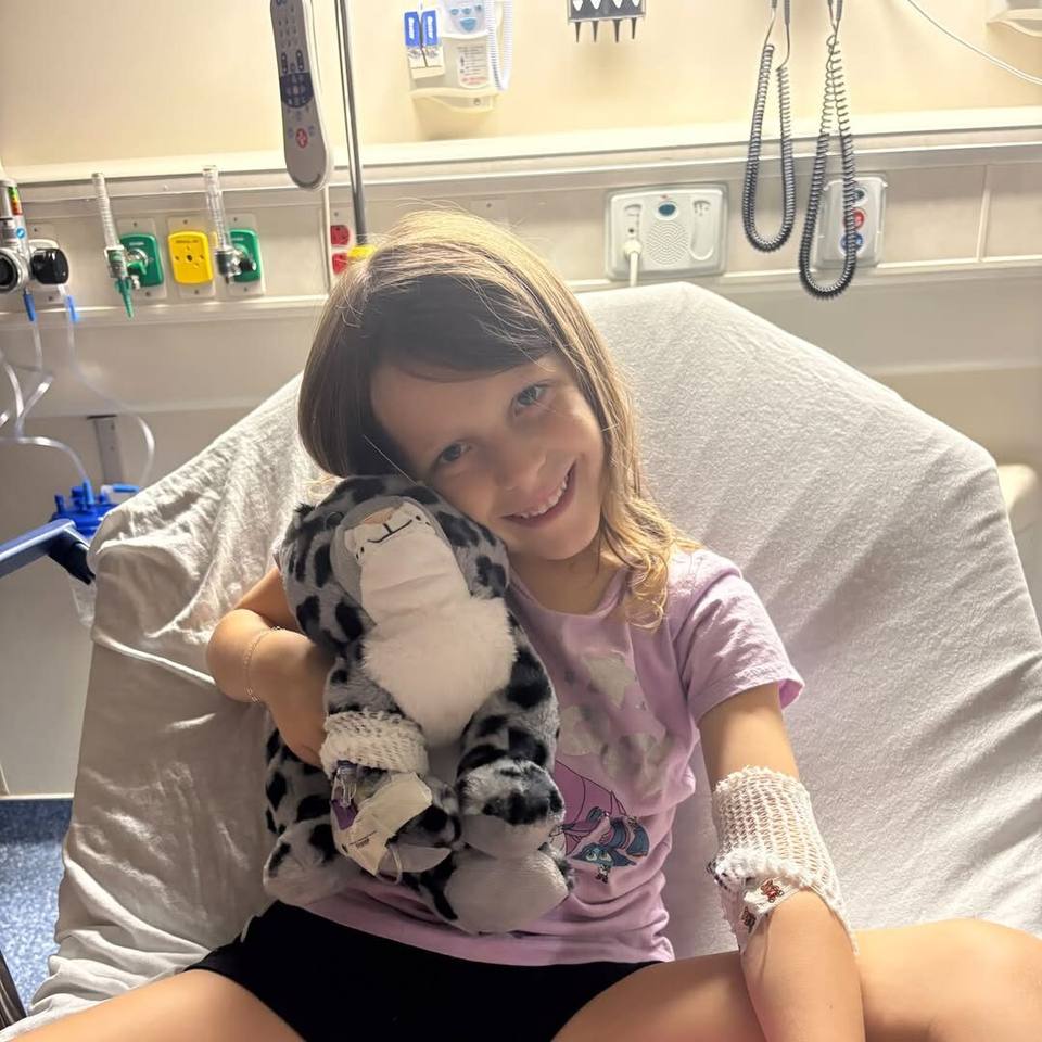 Grace Welker smiles in her hospital bed at Monroe Carell Jr. Children's Hospital, hugging a stuffed snow leopard.