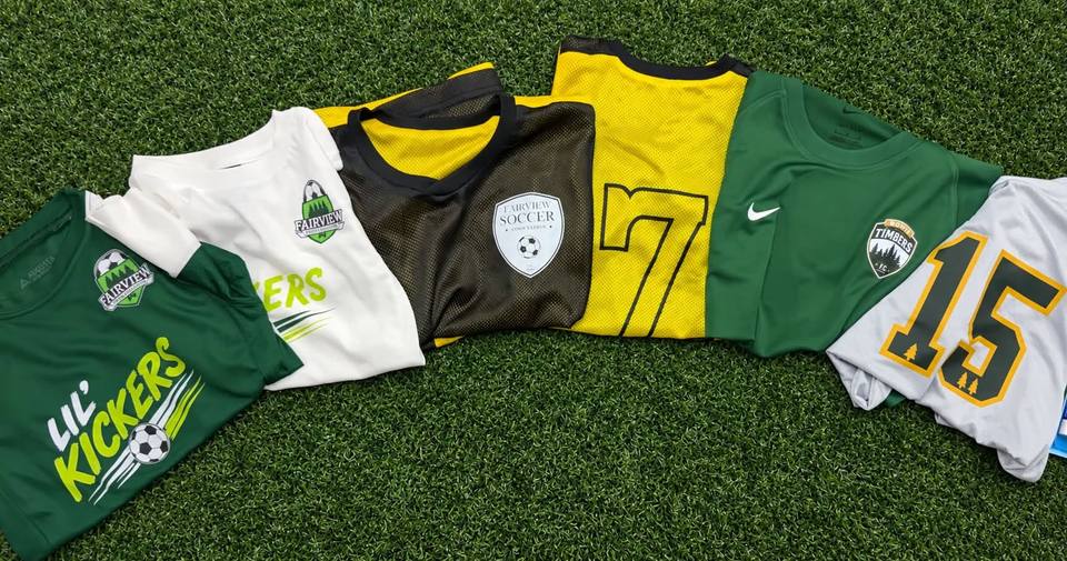 Youth soccer jerseys for Lil' Kickers, Fairview Soccer Association and Bowie Timbers FC laid out on artificial turf.