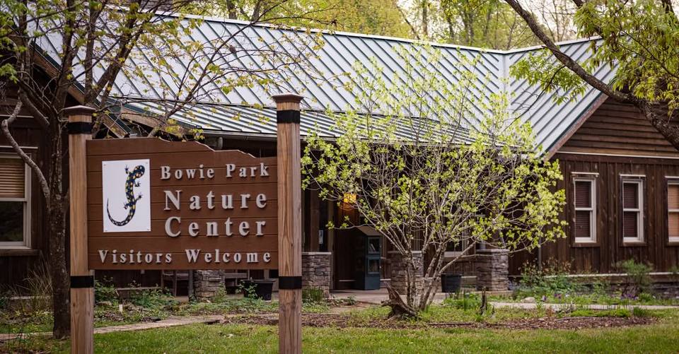 The wooden Bowie Park Nature Center sign stands in front of the park's nature center building.
