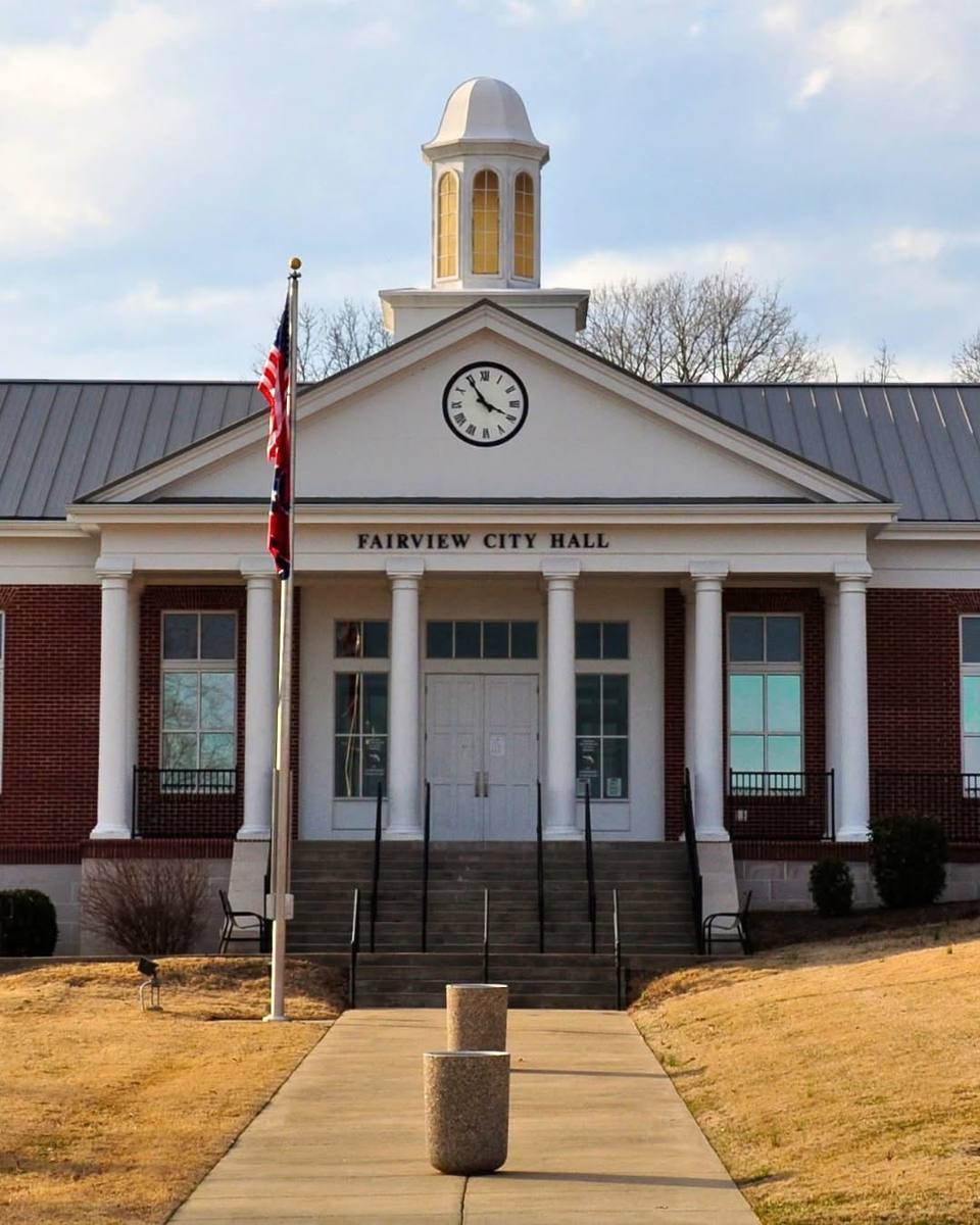 Photo of Fairview City Hall, a brick building with white columns, a pediment clock and a domed cupola.