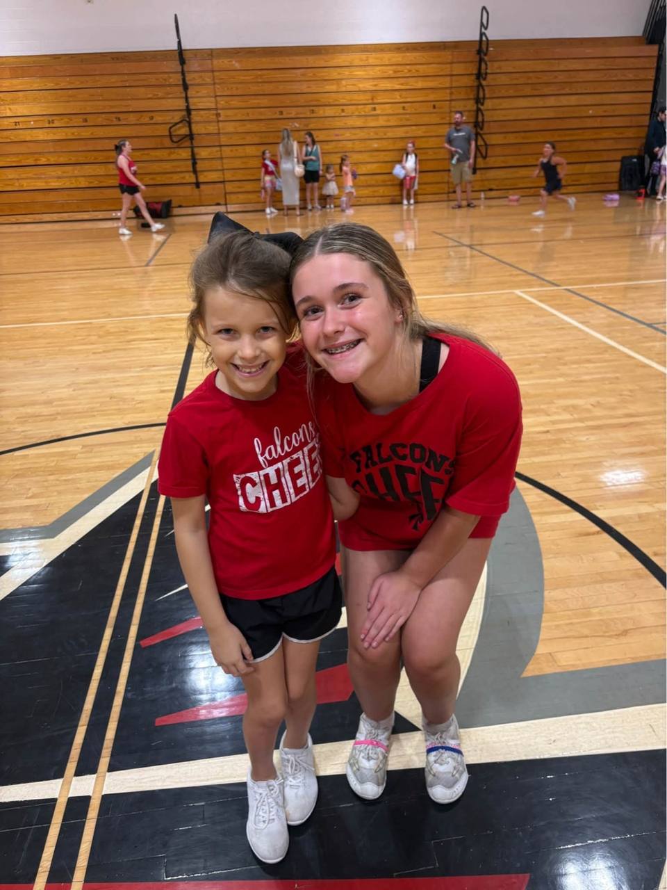 Grace in a red Falcons cheer shirt standing beside a Fairview Middle School cheerleader in a gym.