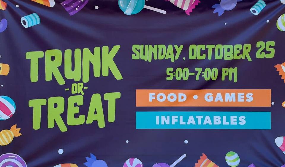 A dark purple Trunk or Treat banner in bright green lettering, bordered with cartoon candies and lollipops, listing the date, time, food, games and inflatables.