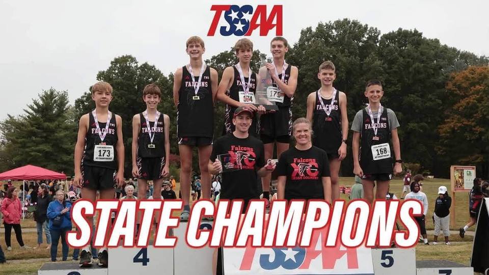Seven Fairview Middle boys cross country runners in black Falcons uniforms and medals stand on a podium with two coaches, under a TSSAA logo and the words State Champions.